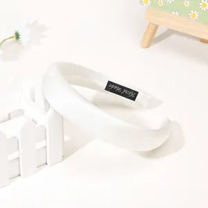 Detail of white satin headband with soft pearl luster and black Hand Made woven label
