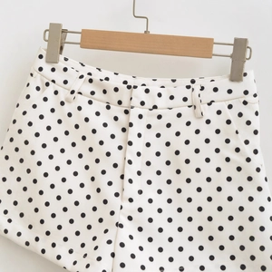 High-waisted white shorts with black polka dot pattern displayed on a wooden hanger