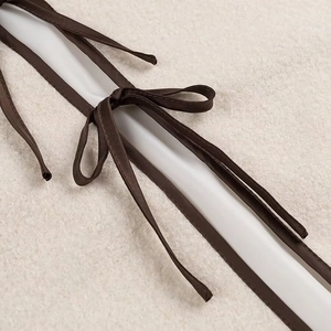 Detail of brown contrast binding and knotted tie on white faux shearling jacket