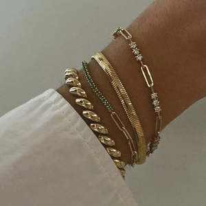 Close-up of gold layered bracelets including tennis chain and green gemstone on woman wrist