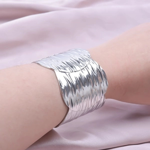 Close-up of a wide silver cuff bracelet with irregular vertical wave textures on wrist