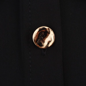Detailed macro view of a hammered gold button on black twill sleeveless dress fabric