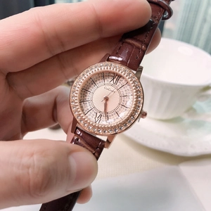 Detail of rose gold rhinestone watch with brown leather strap and roman numeral dial