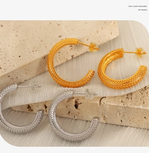 Detailed macro shot of C-shaped hoop earrings with woven texture on beige travertine