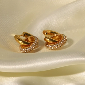 Elegant gold-tone twist hoop earrings with clear pavé zircon on silk fabric background
