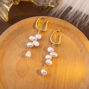 Macro detail of Baroque style gold ear clips with irregular white pearls on a wooden tray