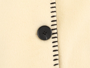 Detailed macro view of beige wool fabric texture with black button and contrast stitching