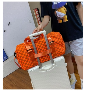 Detail of orange checkered travel bag with sleeve attached to white suitcase handle