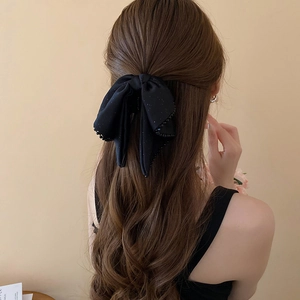 Detail of a large black bow hair claw with subtle glitter on long wavy hair back view