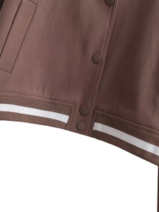 Detail view of tan baseball jacket featuring color-matched snap buttons and striped hem