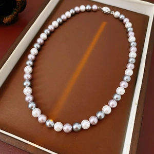 Close-up of multicolor pearl necklace with white, pink, and grey pearls on leather tray
