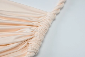 Detailed close-up of apricot pleated fabric with twisted rope shoulder strap design