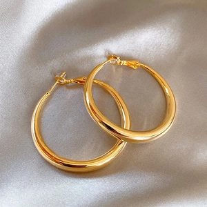 Close-up of oversized golden hoop earrings on elegant silver silk fabric background