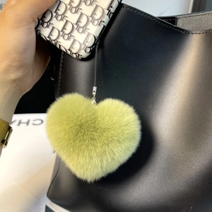 Light green heart-shaped rabbit fur keychain pendant hanging on a black leather handbag