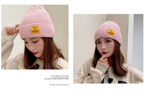 Detailed close-up of pink knitted beanie featuring a yellow ambitious letter patch