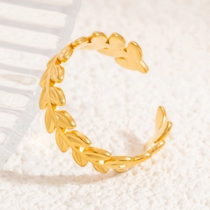 Detailed close-up of golden adjustable olive leaf ring on white textured fabric background