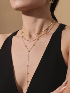 Détail de colliers dorés superposés avec pendentif coeur et zircone sur vêtement noir