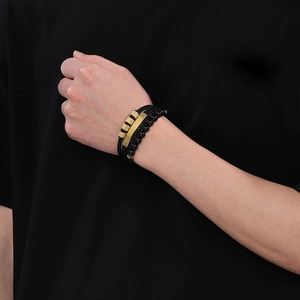 Detail of men's multi-layer bracelet featuring black beads and gold-tone curved metal plate