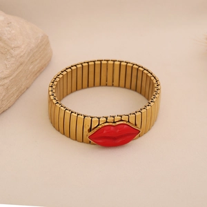 Detail of golden elastic watch-band bracelet with a vibrant red lip enamel charm center
