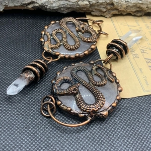Detailed shot of bronze snake earrings with clear crystal hexagon prism pendant