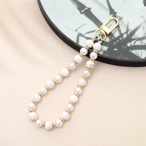 Detailed close-up of white turquoise beads and pearls with golden metal accents on a phone strap
