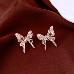 Detailed close-up of bow earrings with pink and green stones on luxury red silk