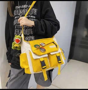 Detail of canvas messenger bag with yellow buckle, dinosaur charm and pins decoration
