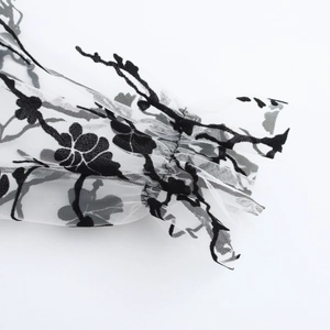 Close-up of white mesh sleeve with black flocked patterns and elegant ruffled cuffs
