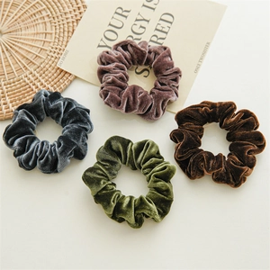 Flat lay view of four velvet scrunchies in dark grey, pink, dark green, and brown tones