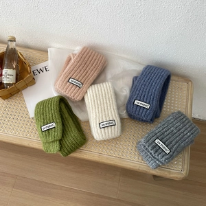 Assorted knit scarves in pink, green, cream, blue and grey displayed on a wooden bench