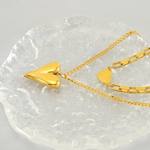 Close-up of double-layered gold heart necklace with glossy finish on water-textured glass