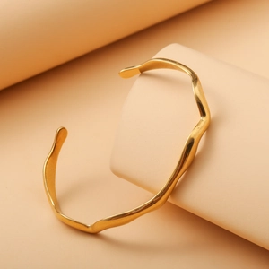 Detail of elegant gold wavy stainless steel open cuff bracelet with water ripple texture