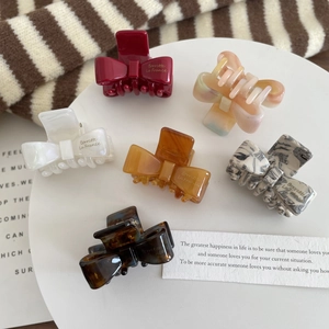 Set of six colorful bow-shaped acetate hair claws on a decorative white tray