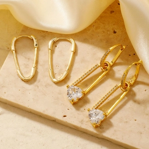 Elegant gold safety pin earrings with sparkling heart-shaped zircon on silk background