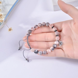 Adjustable hand-woven bracelet with pink zebra stone beads and compass charm on wrist