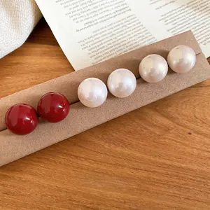 Elegant red and white pearl stud earrings set on a velvet display with a warm vintage backdrop