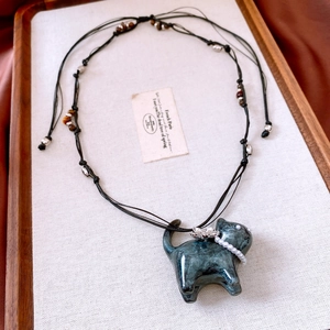Detailed view of dark green cat pendant necklace with pearl collar and floral accent