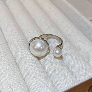 Macro shot of silver open ring with dual white pearls on a beige textured jewelry box