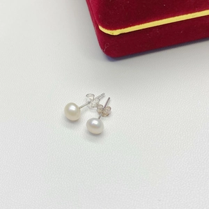 Macro detail of elegant round white pearl earrings with silver metal posts on leather