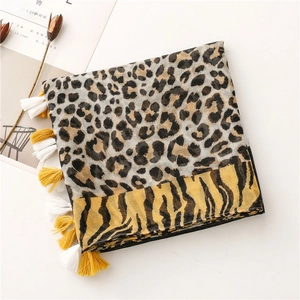 Detail of leopard and tiger print scarf with vibrant yellow tassels on a white surface
