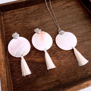 Bohemian jewelry set with round shell pendants and ivory silk tassels on dark wood tray