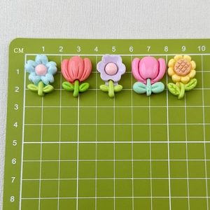 Close-up of assorted resin tulip and sunflower cabochons for DIY hair clips on a green cutting mat