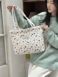 Detail of white quilted tote bag featuring cute cartoon animal prints and a blue woven label
