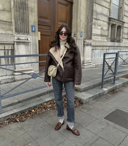 Photo en extérieur d'une veste en peau lainée marron avec un jean gris et un sac beige
