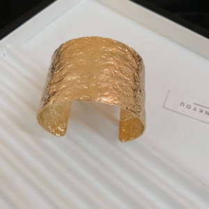 Macro shot of gold wide open cuff bracelet featuring an irregular hammered metal texture