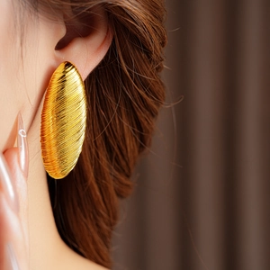 Detail of gold oval hoop earring with brushed texture shown on a female model