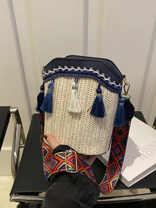 Detail of woven straw bucket bag featuring blue fringe tassels and ethnic patterned strap