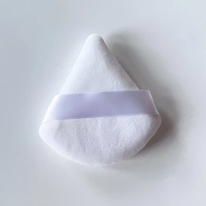 Detail of a large white triangular powder puff with a soft velvet texture and satin ribbon