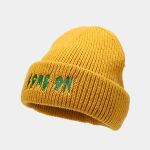 Dettaglio del berretto in maglia gialla con ricamo COME ON verde e trama in maglia spessa