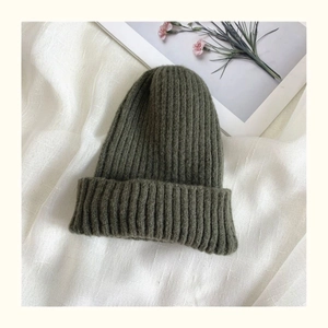 Detail of dark olive green ribbed knit beanie with soft texture on a textured fabric base